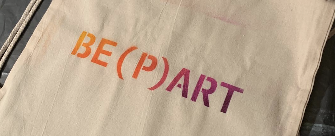 Ein Jutebeutel mit dem Schriftzug beharrt in orange und lila.